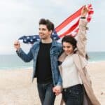 a man and woman walking on a beach holding an american flag