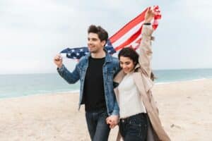 a man and woman walking on a beach holding an american flag
