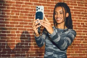 Smiling woman takes a selfie with smartphone against brick wall.