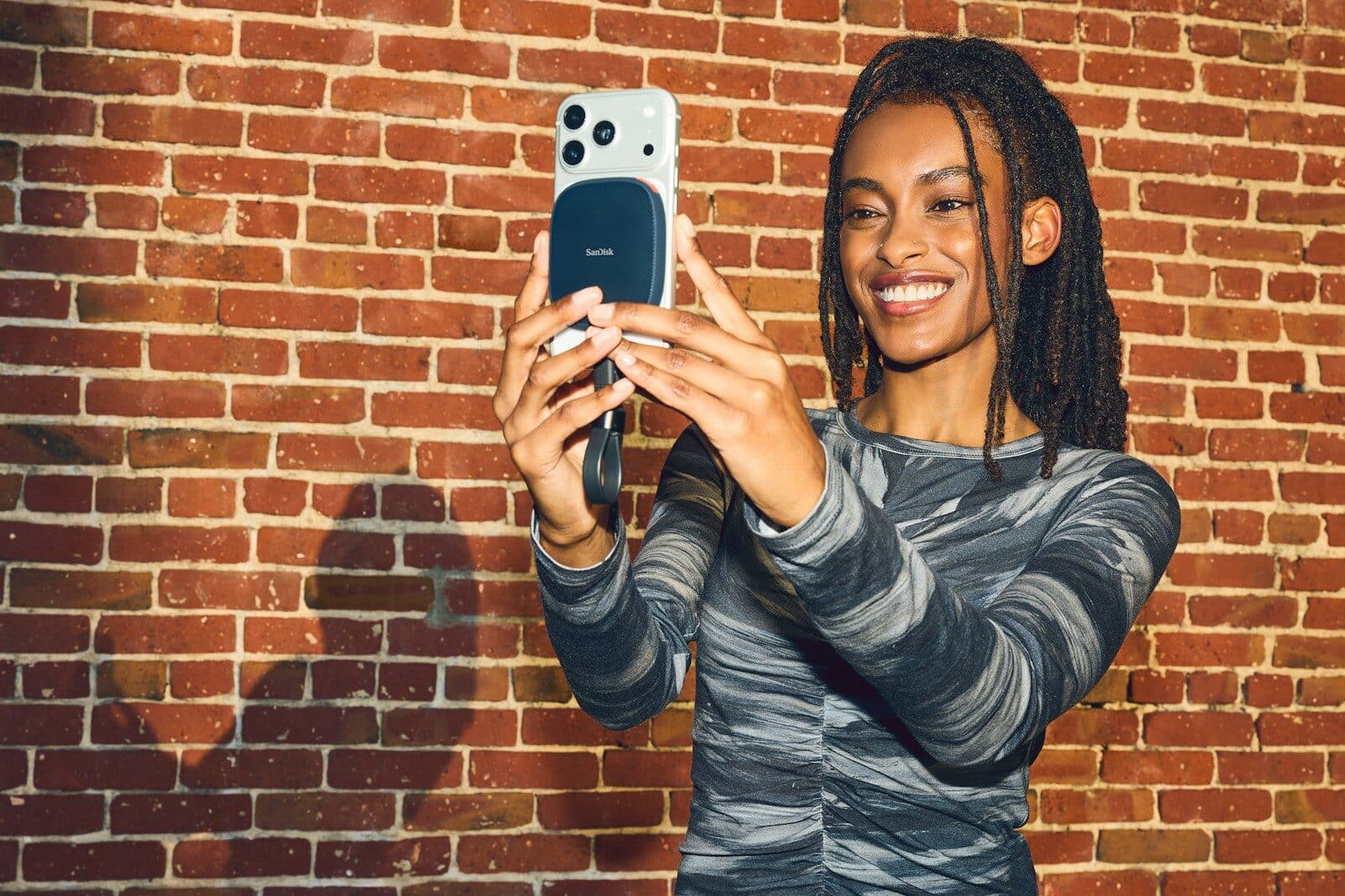 Smiling woman takes a selfie with smartphone against brick wall.