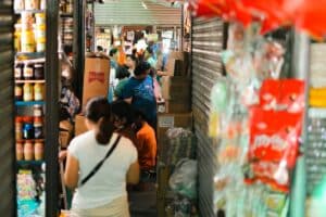 A crowded indoor market with people shopping and stocked shelves.