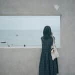 Woman in long dress looking out window at ocean