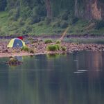 Une tente sur une plage, près d'un lac, avec un pêcheur